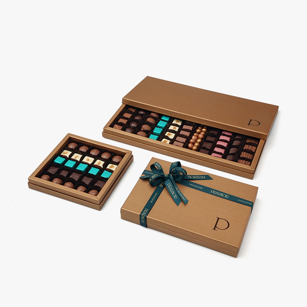 Prestige Supremo Laissez-vous séduire par l'élégance de ce coffret et l'authenticité des chocolats, créant ainsi une expérience gourmande inoubliable pour les amateurs de chocolat les plus fins. Savourez notre assortiment de <strong>750g </strong>offrant 11 variétés de saveurs exquises présenté dans un emballage rigide à l'effet cuir. 2 Prestige Supremo – Image 2
